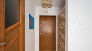 A hallway with a wooden door, a wall-mounted light fixture, and a tiled floor.