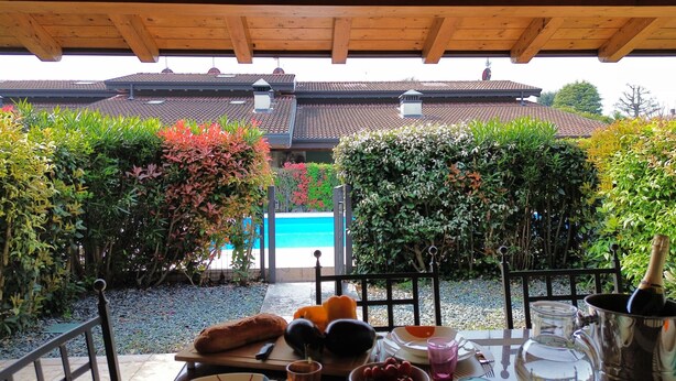 A patio with a table set for a meal, a pool, and a building with a tiled roof in the background. - Maison Belvedere By Bookinggardalake (Manerba del Garda)