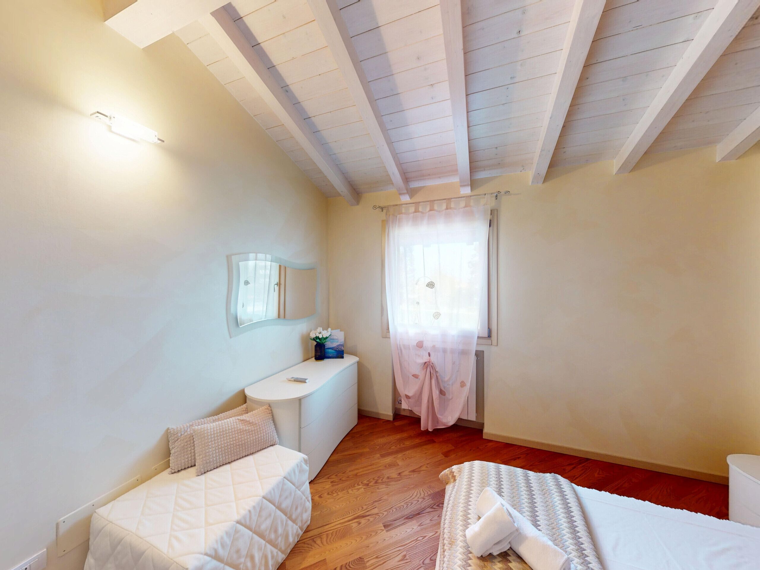Une chambre à coucher comprenant un lit, une table de chevet, un miroir, une fenêtre avec des rideaux et un plancher en bois.
