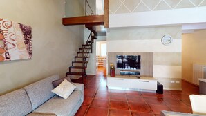 A living room with a sofa, a fireplace, a staircase, and a clock on the wall. - Maison Belvedere By Bookinggardalake (Manerba del Garda)