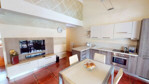 A modern kitchen with a dining area, featuring a flat-screen TV, a coffee machine, and a built-in oven. - Maison Belvedere By Bookinggardalake (Manerba del Garda)