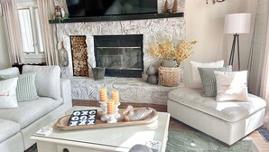 A cozy living room with a stone fireplace, comfortable sofas, a coffee table with decorative items, and a mounted fish on the wall. - Lake House Cabin 3BR/2BA Sleeps 6 Water Front With Private Boat Dock for Fishing (Cedar Bluff)