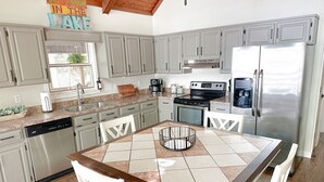 A modern kitchen with grey cabinets, a stainless steel refrigerator, a built-in oven, and a coffee maker. - Lake House Cabin 3BR/2BA Sleeps 6 Water Front With Private Boat Dock for Fishing (Cedar Bluff)