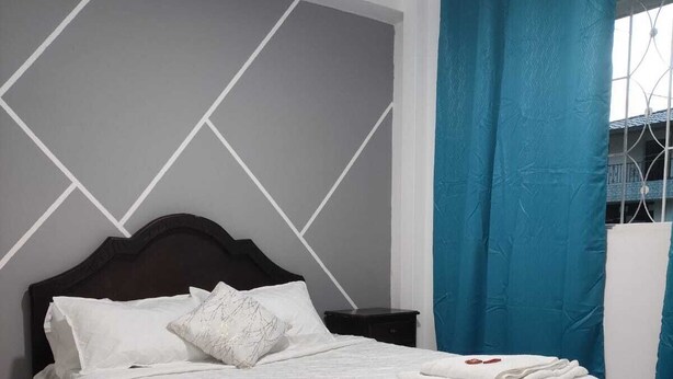 A neatly made bed with a white bedspread and pillows, a dark wooden headboard, and a blue curtain on a window. - Hotel zocalos y colores (Guatape)