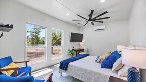 Une chambre moderne avec un lit, un bureau, une chaise, un téléviseur et de grandes fenêtres.