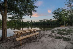 A wooden picnic table by a calm lake with trees in the background.