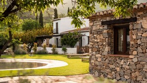 A stone building with a window, surrounded by a well-maintained lawn and a circular stone pathway. - Cortijo Rural Fandango 3 - Pool and Mountain (Almuñecar)