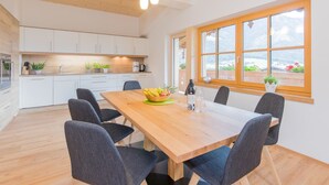 A modern kitchen with white cabinets, a wooden dining table, and a large window with a view of mountains.
