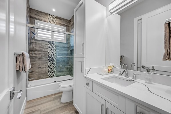 A modern bathroom with a glass shower enclosure, a white toilet, and a vanity with a sink and mirror. - New! Seashell Oasis - 3 Ensuites! 1 Mile to the Beach! - Heated Pool! (Naples)
