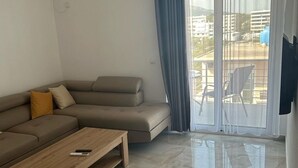 A modern living room with a beige sectional sofa, a wooden coffee table, and a sliding glass door leading to an outdoor area.