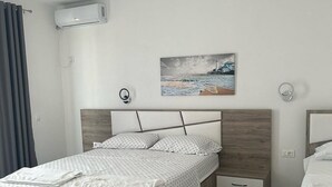A bedroom with a bed, a bedside table, a nightstand, a wall-mounted air conditioner, a painting, and a window with curtains.