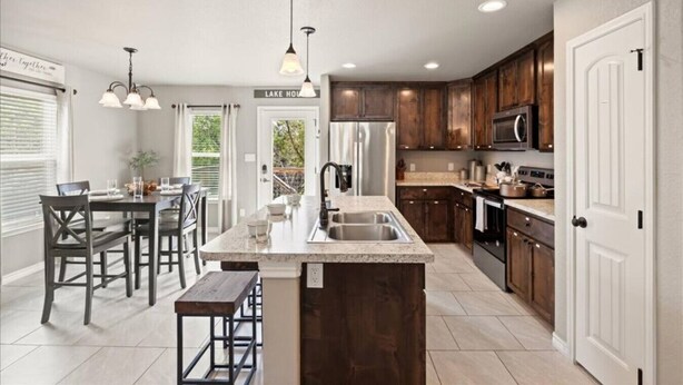 A modern kitchen with dark wood cabinets, a granite countertop, stainless steel appliances, and pendant lighting.
