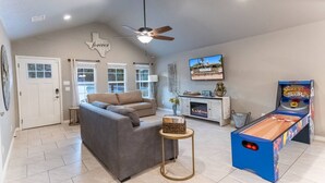 A living room with a sofa, a coffee table, a television, and a shuffleboard table.