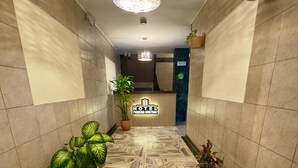 Un'hall d'albergo con una reception, piante in vaso, un pavimento decorato e una lampada a sospensione.