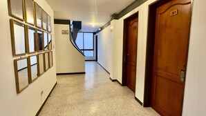 Un corridoio con pavimento lucido, una serie di specchi incorniciati sulla parete sinistra e porte in legno alla destra.