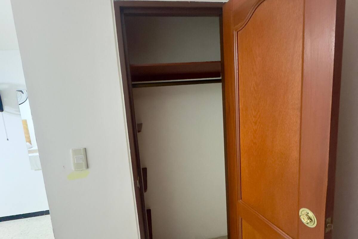 Um quarto com porta de madeira, parede branca e chão de azulejos.