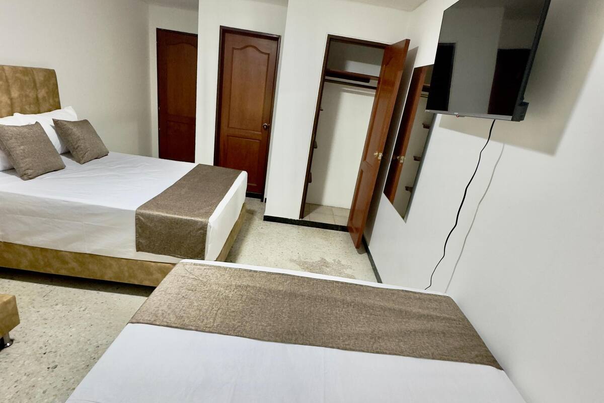 Quarto de hotel com duas camas, um guarda-roupa, um espelho e uma luminária no teto.