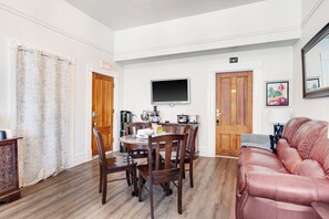 A dining area with a wooden table and chairs, a television mounted on the wall, and a couch with a cushion. - Charming B&B steps to beach, boardwalk, pier, shop, restaurants w bath & WiFi #6 (Santa Cruz)
