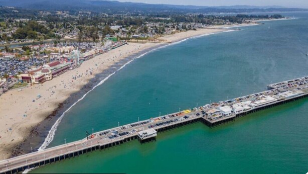 An aerial view of a beach with a pier extending into the ocean, surrounded by buildings and a distant mountain range. - Charming B&B steps to beach, boardwalk, pier, shop, restaurants w bath & WiFi #6 (Santa Cruz)