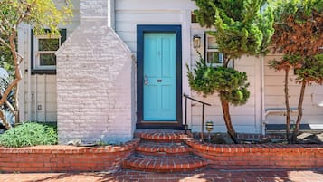 A house with a blue door, a brick chimney, and a small tree in the front yard.