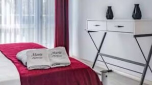A hotel room with a bed, a red bedspread, two towels, a white bedside table with two black vases, and a wall clock. - Charming B&B steps to beach, boardwalk, pier, shop, restaurants w bath & WiFi #6 (Santa Cruz)