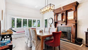 A room with a wooden dining table, red chairs, a fireplace, and a large window with a view of trees.