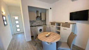 A compact living space with a dining area, kitchenette, and a flat-screen TV mounted on the wall.