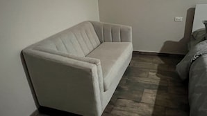 Ein Eckzimmer mit einem beigefarbenen Sofa, einem Bett mit gemusterten Bettwäsche und einem Fliesenboden.
