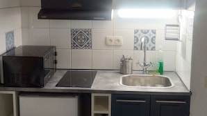 A compact kitchen with a refrigerator, stove, sink, and dark cabinets.
