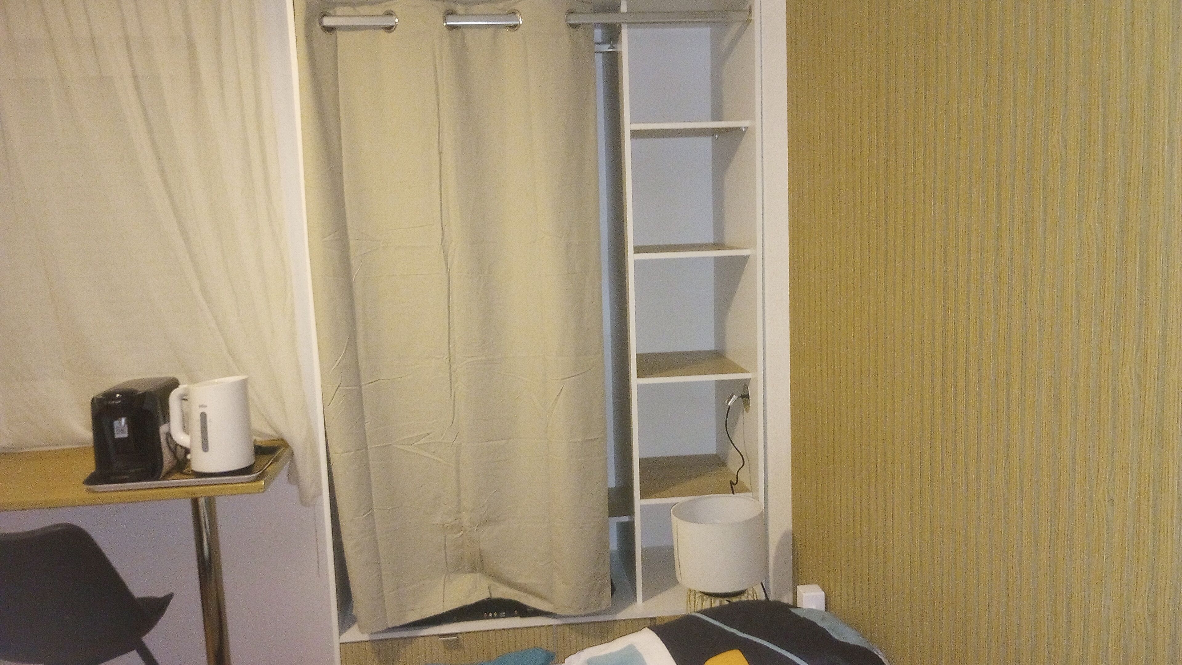 Een kleine badkamer met douchegordijn, een plank met toiletartikelen en een koffiezetapparaat op een tafeltje.