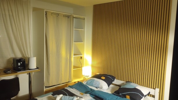 A hotel room with a bed, bedside table, lamp, and a curtain.