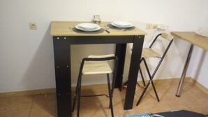 A small dining table with two plates and a knife, a folding chair, and a wall socket.
