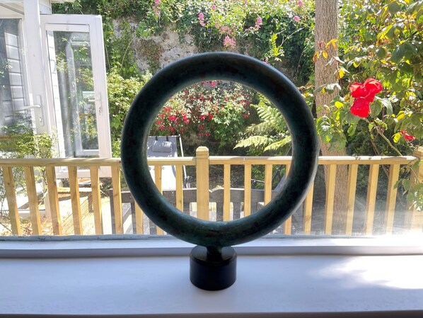 Un oggetto circolare su un davanzale con vista su un balcone, una ringhiera in legno e del verde.
