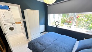 Un dormitorio con cama, armario, lavadora y ventana con vistas a zonas verdes.