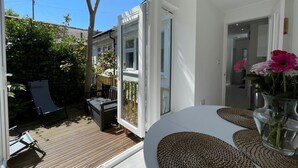 Una habitación moderna con un amplio ventanal corredera que da a una terraza exterior, una mesa redonda con individuales tejidos y un jarrón con flores.