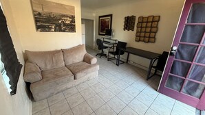Un salon avec un canapé beige, un bureau avec un ordinateur et une porte avec une fenêtre.