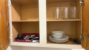 Un buffet en bois, doté d’étagères où sont rangés des verres à boire transparents, des assiettes blanches et des couverts.