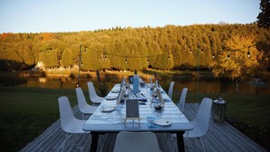 A wooden deck with a table set for six, overlooking a lake and forest. - Exclusive 100-Acre Modern Estate Designed Home (Alton)