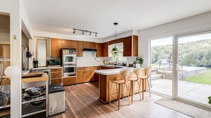 A modern kitchen with wooden cabinets, stainless steel appliances, and a large island with bar stools. - Exclusive 100-Acre Modern Estate Designed Home (Alton)