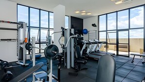 A modern gym with various exercise equipment, large windows, and a view of the sky. - 1 quarto, cheio de estilo, condo club Sky com vaga (Curitiba)