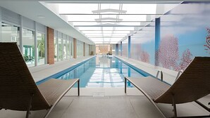 Ein moderner Innenpool mit Glaswänden, Liegestühlen und einem Wandbild von Korallenriffen.