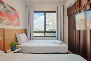 Een hotelkamer met een bed, een tafeltje met een plant, een raam met gordijnen en uitzicht op de stad.