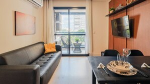 A modern living room with a sofa, a dining table with a TV, and a balcony with outdoor furniture. - Oásis Urbano com Vistas Deslumbrantes no Sky CWB (Curitiba)