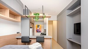 A modern hotel room with a bed, a desk with two chairs, a TV, and a painting on the wall. - Studio incrível no condomínio clube sky Batel soho (Curitiba)