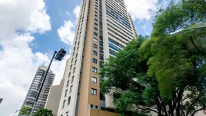 A tall, modern building with multiple floors, surrounded by trees and a clear sky. - Studio incrível no condomínio clube sky Batel soho (Curitiba)