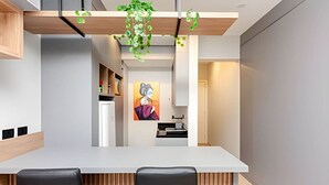 A modern kitchen with a white countertop, black chairs, and a hanging plant. - Studio incrível no condomínio clube sky Batel soho (Curitiba)