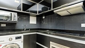 Una cocina moderna con lavadora y secadora integradas, un salpicadero de azulejos negros y una encimera de acero inoxidable.