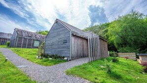 Een rustiek houten gebouw met schuin dak, omringd door een grindpad en weelderige begroeiing.