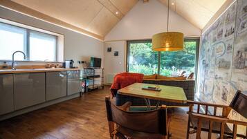 A modern kitchen with a dining area, wooden flooring, and a large window providing a view of greenery.