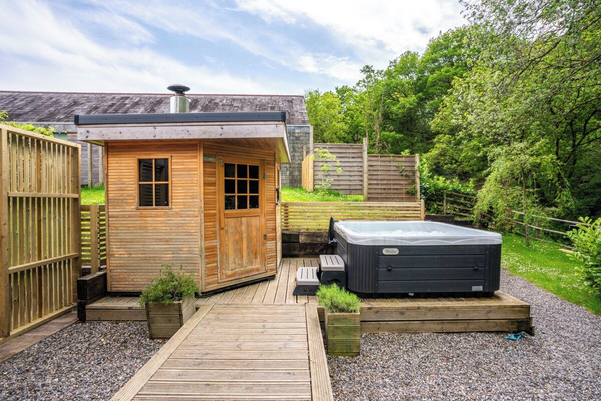 Een houten loungetuin met een jacuzzi, een houten terras en omliggende beplanting.